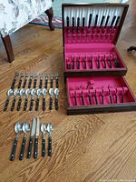 Full view of the set showing two wooden drawers open, filled with cutlery pieces organized in red velvet compartments, and additional utensils laid out on the floor.