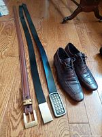 Photo showing brown croc-embossed leather dress shoes with three leather belts of different styles and colors laid out on wooden floor