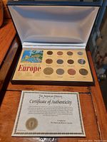 Open blue box displaying 12 coins in a colorful holder with country names and map, showing The Last Coins of Europe set.