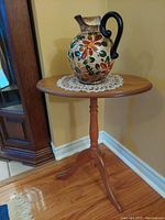 Photo of the vintage tilting small oval table showing the oak finish top with a decorative vase placed on a lace doily.