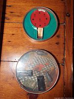 Top view of red paddle coordination toy with white balls and numbered holes on green background.