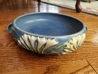 Side angle view of blue vintage Roseville handled bowl with raised freesia floral relief.