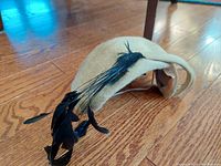 Top angle side view of the beige hat placed on wood floor showing black feather decoration.