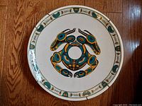 Top view of the painted pottery art plate showing Haida beaver design and border, with visible edge chip repaired with epoxy.