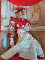 Front view of the Soda Fountain Sweetheart Barbie doll dressed in white and red, seated with dress flowing, holding a Coca-Cola glass.