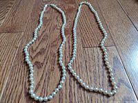 Photo showing both vintage cultured pearl strands laid out on a wood floor, highlighting the overall length and bead arrangement.