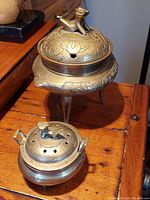 Both brass Foo Dog lidded incense pots, one small with handles, one larger with tripod legs and engraved decorations