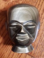 Front view of hand sculpted obsidian man head sculpture showing geometric facial carvings and natural color variations of volcanic glass.