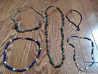 Group photo showing five vintage stone necklaces lying on a wooden surface, displaying various bead colors, shapes, and sizes.