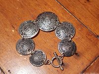 Full image of the bracelet showing seven connected circular discs etched with Mayan calendar designs and toggle clasp.