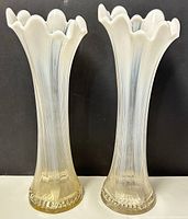 Front view of two Fenton swung French reverse opalescent glass vases showing the full height and shape, placed on a white surface against black background.