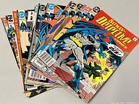 Stack of 15 Batman Detective Comics issues showing front covers featuring Batman in various poses including an issue with Batman shooting a grappling gun.