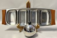 View of the entire lot with the stainless steel serving tray displayed horizontally showing its four divided compartments and wooden handles, with the spherical sugar bowl placed in front, showing its cover, spoon, and small black knob.
