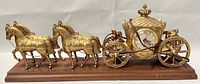 Full side view showing the gold-tone horses and coach with clock mounted on a wooden base.