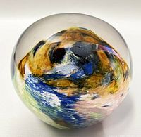 Close-up photo of spherical art glass paperweight showing colorful swirls in yellow, blue, black, and green inside clear glass.