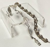 Two sterling silver bracelets displayed on clear stands to show design and length.