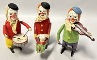 Front view of three clown figures: drummer, balancing, and violinist