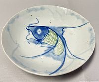 Top-down view of round porcelain plate showing full koi fish design on the surface with blue and green coloring.