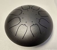 Top view showing the black steel tongue drum with 10 tonal tongues cut in symmetrical petal shapes.