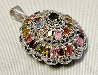 Front angled view of round, tiered pendant showing arrangement of multi-colored faceted stones.