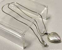 Sterling silver snake chain laid out horizontally with the heart locket pendant hanging to the side on clear acrylic stand, showing clasp and chain detail.