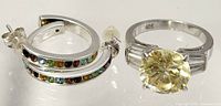 Pair of silver hoop earrings with multicolored crystals and a 925 silver ring with large yellow oval stone flanked by clear baguette stones.