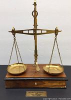 Front view of brass scales showing two hanging pans and wooden base