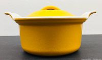 Side view showing bright yellow enamel cast iron pot with white handles and flared rim.
