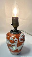 Full view of the lamp showing the hand painted floral design and electric bulb lit.
