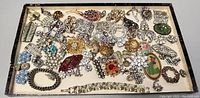 Overview of assorted vintage crystal costume jewelry pieces including brooches, bracelets, and earrings arranged in a display box.