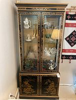 Front view of Drexel Heritage black lacquer chinoiserie display hutch showing glass doors with gold decorations and lower cabinet.