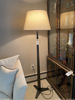 Floor lamp shown illuminated next to couch and cabinet to highlight size, design, and shade detail.