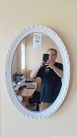 Front view of the oval mirror hanging on a wall with a visible room reflection and a person taking the photo.