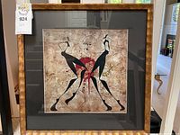 Full view of the framed mixed media print showing the wooden frame, dark mat, and centered print with abstract figures.