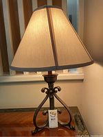 Side view of the table lamp showing the beige fabric shade and metal scrollwork base on wooden surface.