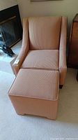 Front angle showing peach upholstered chair and accompanying ottoman placed on carpet.