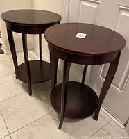 Two dark wood round accent tables positioned side by side on a tiled floor in front of a white door.
