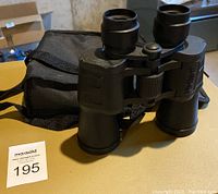 Front view of Vivitar binoculars standing upright on a surface with carrying case behind them.