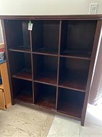 Front and side angle view of rectangular wooden book case with 9 cubby compartments in a 3x3 layout. The book case has medium to dark wood finish and no doors or drawers.