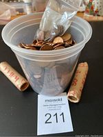 Photo showing a clear plastic bucket filled with loose Canadian pennies, two paper rolls of pennies labeled 50 each, and a small resealable plastic bag with pennies inside the bucket.