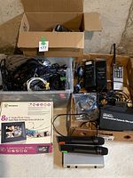Wide view showing overall lot contents including walkie-talkies, digital photo frames in boxes, remote controls, tangled cables in a clear bin, microphones, and receiver units.