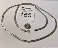 Full view of the silver necklace lying flat with quarter for size comparison and auction lot number card.