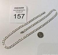 Full view of the sterling silver figaro chain necklace with a coin for size reference.