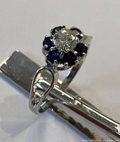 Ring placed on its side showing center diamond, surrounding sapphires and split shank band