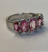 Close-up of silver ring showing five oval pink stones set with small clear stones around each.