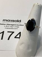 Front view of sterling silver ring with a large dark garnet stone on white display stand.