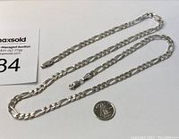 Sterling silver necklace laid flat next to a coin for size reference and a MaxSold auction card.