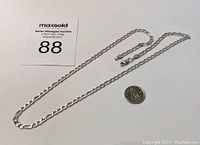 Sterling silver figaro chain necklace next to Canadian quarter for scale, shows full length and clasp