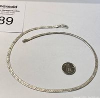 Full view of the sterling silver necklace coiled around a quarter for size comparison.