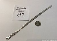 Full view of the twisted link sterling silver bracelet with auction tag and quarter for size reference.